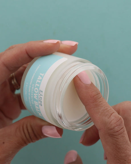 Hand dipping into a jar of unscented tallow against a teal background