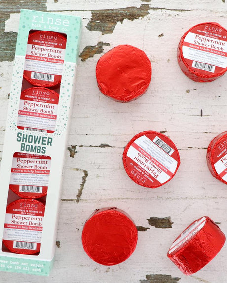 The Peppermint Shower Steamer 4-pack box on chipped white-painted wood with four red foil-wrapped pucks