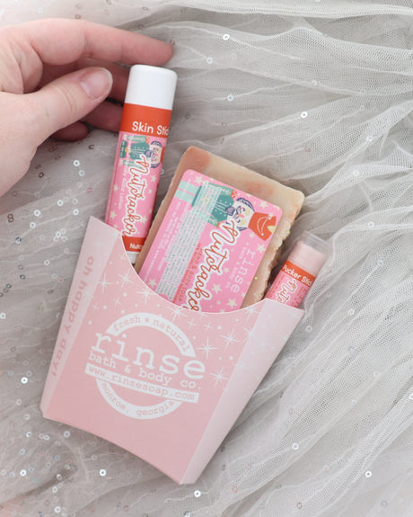 Hand lifting the Nutcracker Skin Stick from a pink fry carton with soap and Pucker Stick on sparkly grey tulle