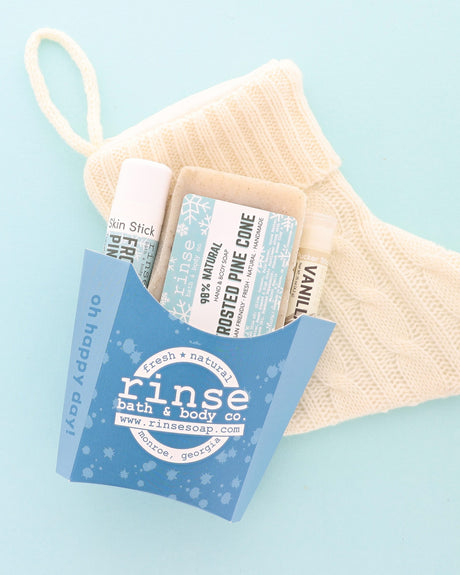 Frosted Pine Cone gift set in a blue fry carton with soap, Skin Stick and Pucker Stick beside a cream knit stocking