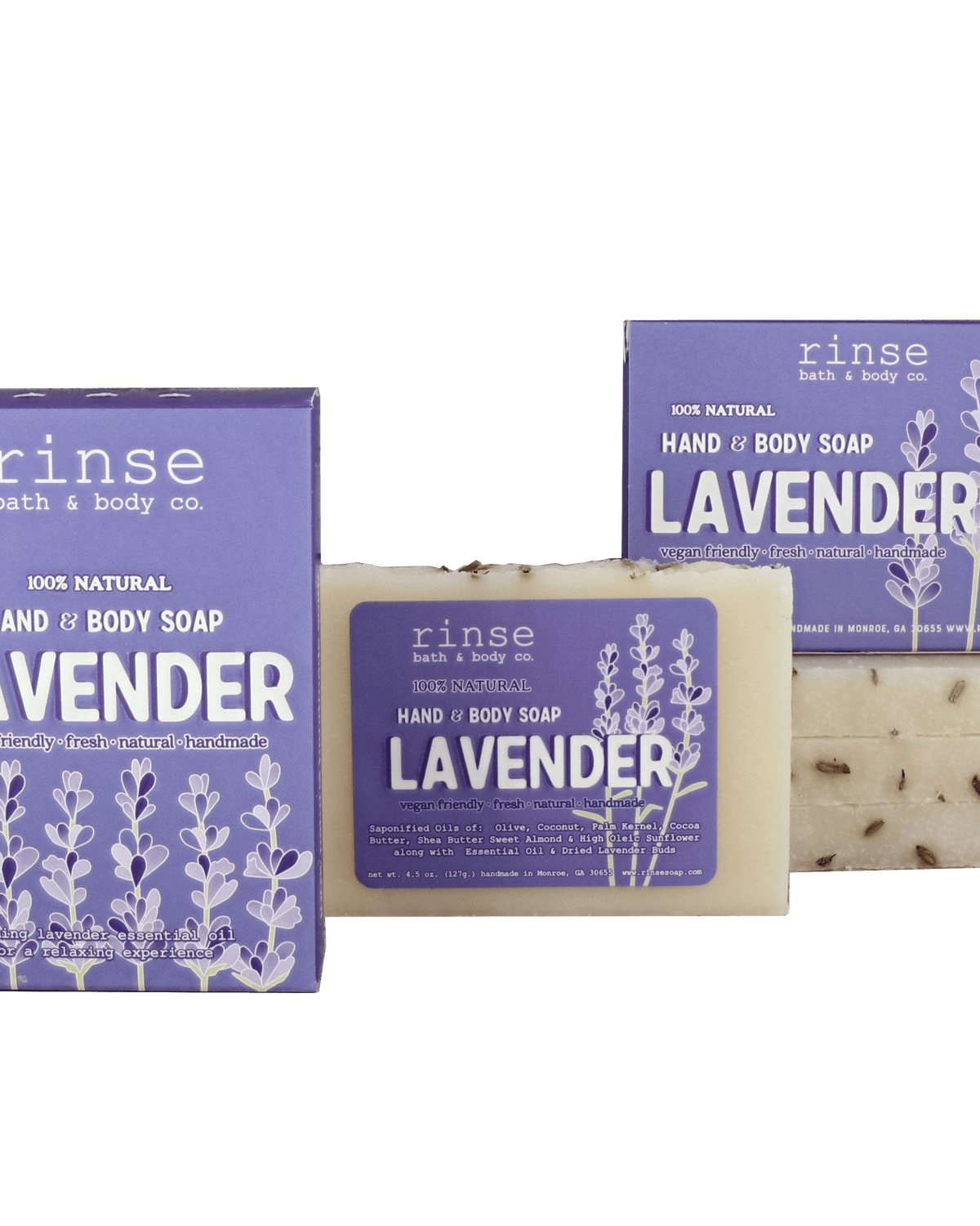 Two purple Lavender soap boxes and a flecked cream bar resting on deep green — botanical buds catching soft studio light