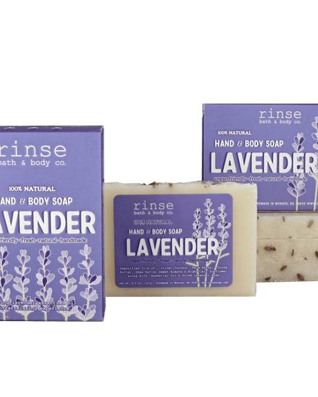 Two purple Lavender soap boxes and a flecked cream bar resting on deep green — botanical buds catching soft studio light