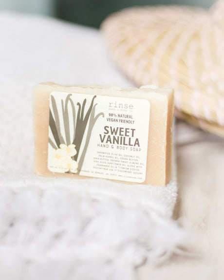 Sweet Vanilla mini soap resting on a white fringe towel — soft sunlit blur of woven basket behind