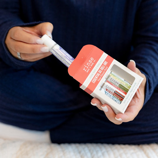 Hands sliding a roll-on from the Four Flavor Pack box — navy sweater sleeves in soft white light