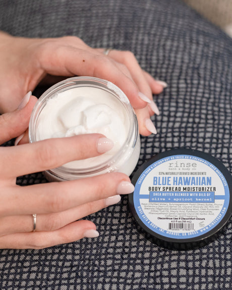 Two hands twisting open a jar of Blue Hawaiian Body Spread, blue label facing the camera