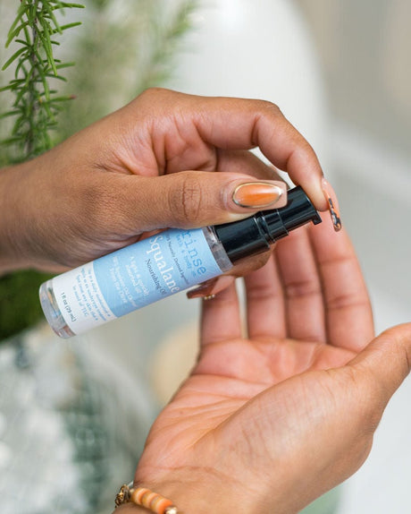 Hand holding a small bottle of squalane oil with a blue label against a blurred natural background