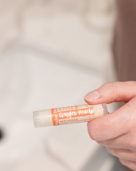 Ginger Peach lip balm held in soft daylight — juicy peach and warm ginger in a cocoa-butter balm for chapped lips. Rinse Bath & Body Co.