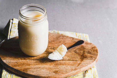 Mason jar of yogurt with a spoonful on a wooden board against a gray background