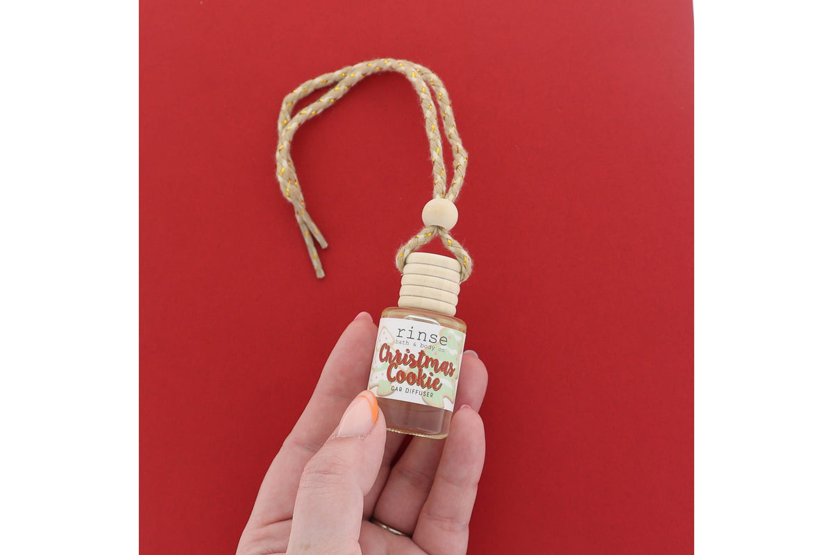 Hand holding Christmas Cookie car diffuser on saturated red — wood cap and jute cord in festive light