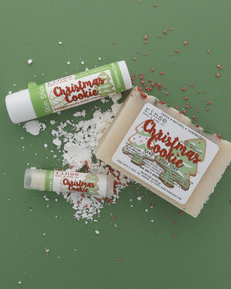 The Christmas Cookie gift set on sage paper scattered with snow and red-and-white sprinkles — bar soap, solid lotion skin stick and lip balm. Rinse Bath & Body Co.