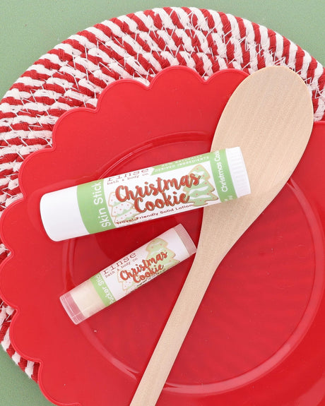 Christmas Cookie Skin Stick and Christmas Cookie Pucker Stick on a red scalloped plate with a wooden spoon