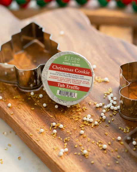 A Christmas Cookie Tub Truffle on a wooden board with metal cookie cutters and scattered gold and white sprinkles — the house smells like December. Rinse Bath & Body Co.
