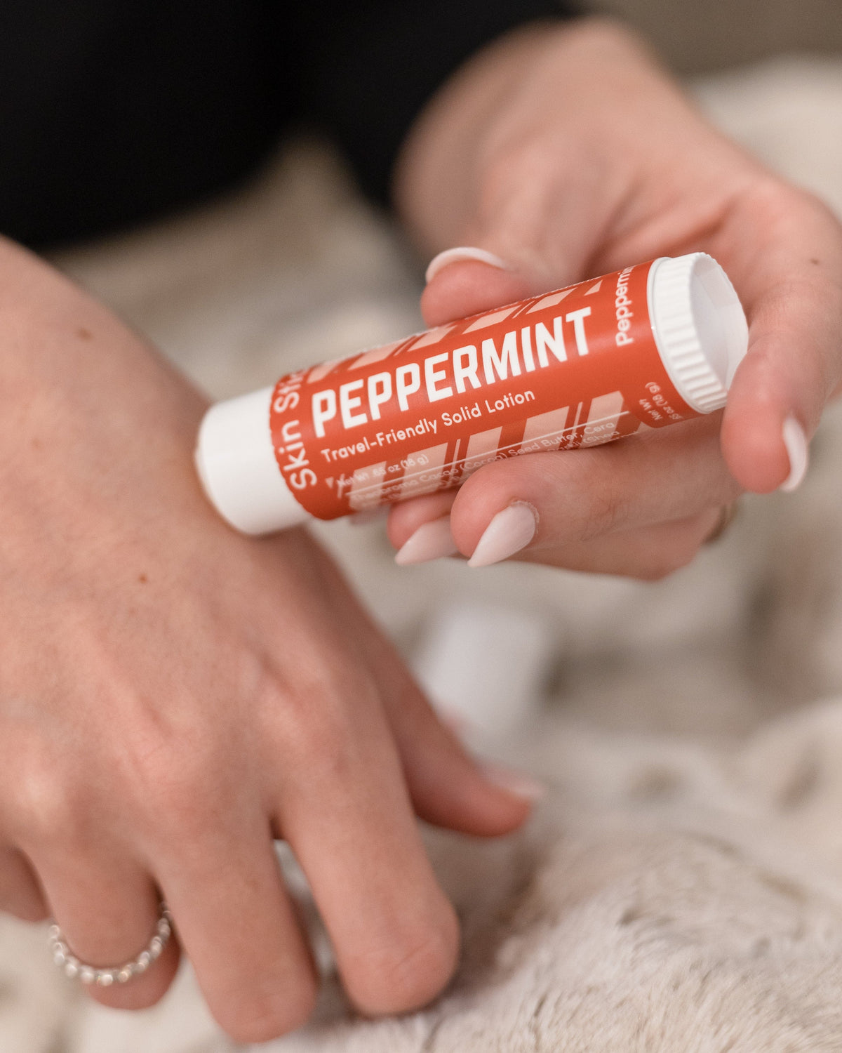 Peppermint Skin Stick in-use on skin — hands gliding solid lotion onto the back of a hand in warm light