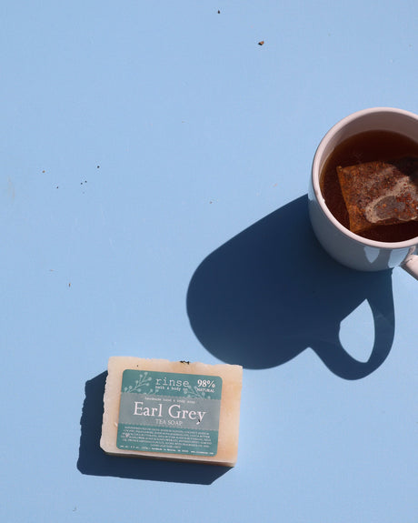 Earl Grey Tea Soap beside a peach mug of steeping tea — long sun shadows on pale blue