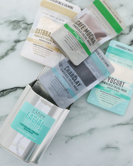 All four masks in the Face Mask Gift Set — Dead Sea Mud, CharClay, Oatbrasion and Cafe Mocha — laid out on marble. Rinse Bath & Body Co.