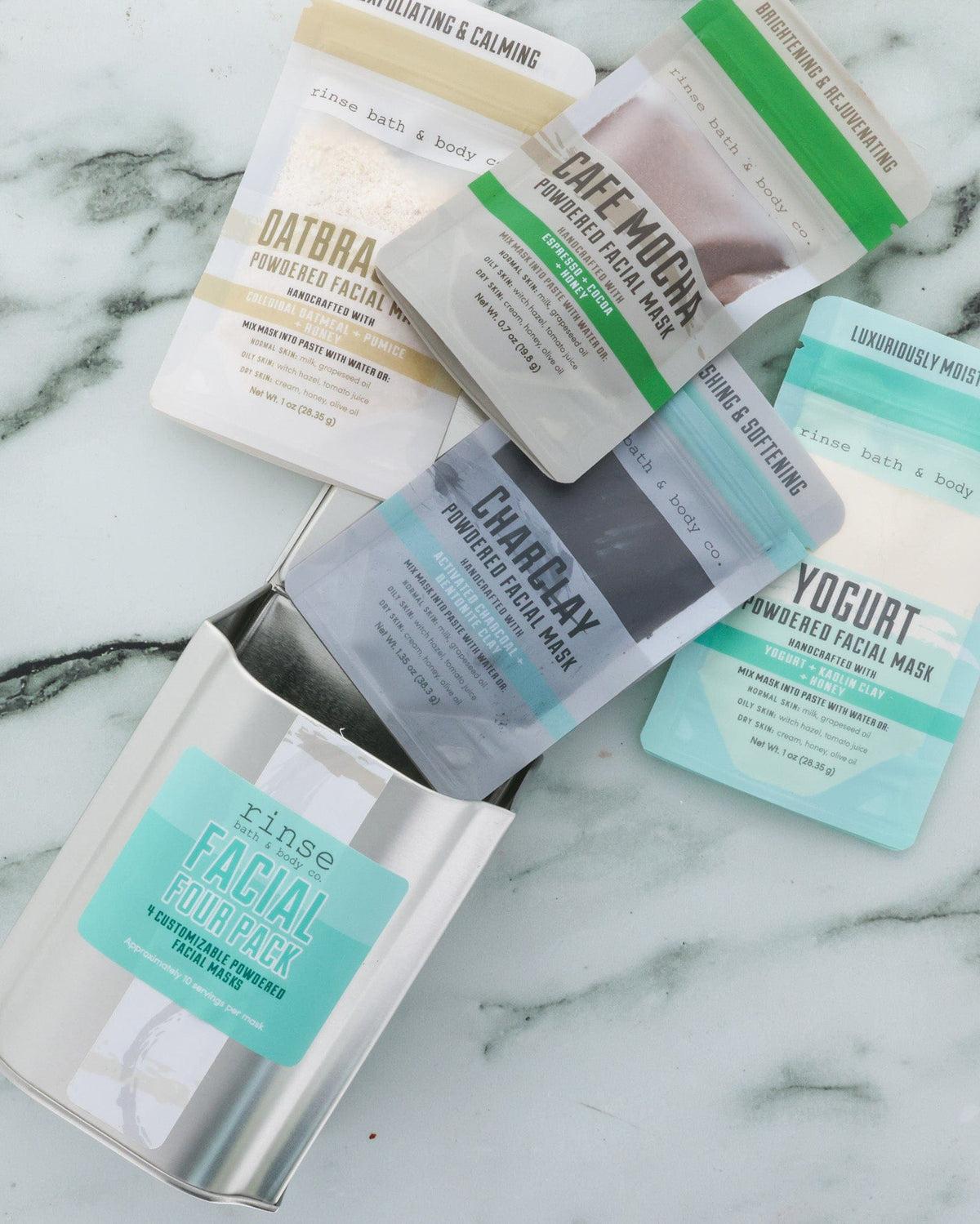 All four masks in the Face Mask Gift Set — Dead Sea Mud, CharClay, Oatbrasion and Cafe Mocha — laid out on marble. Rinse Bath & Body Co.