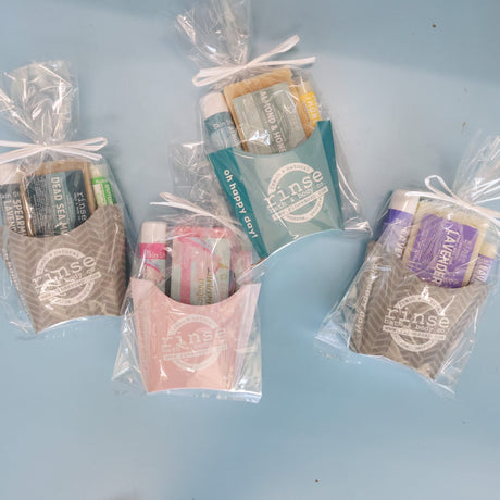 Everyday fry bundles arranged on a pale blue surface — Dead Sea Mud, Almond & Honey, Unicorn Magic and Lavender, cello-wrapped and ready for the shelf. Rinse Bath & Body Co.