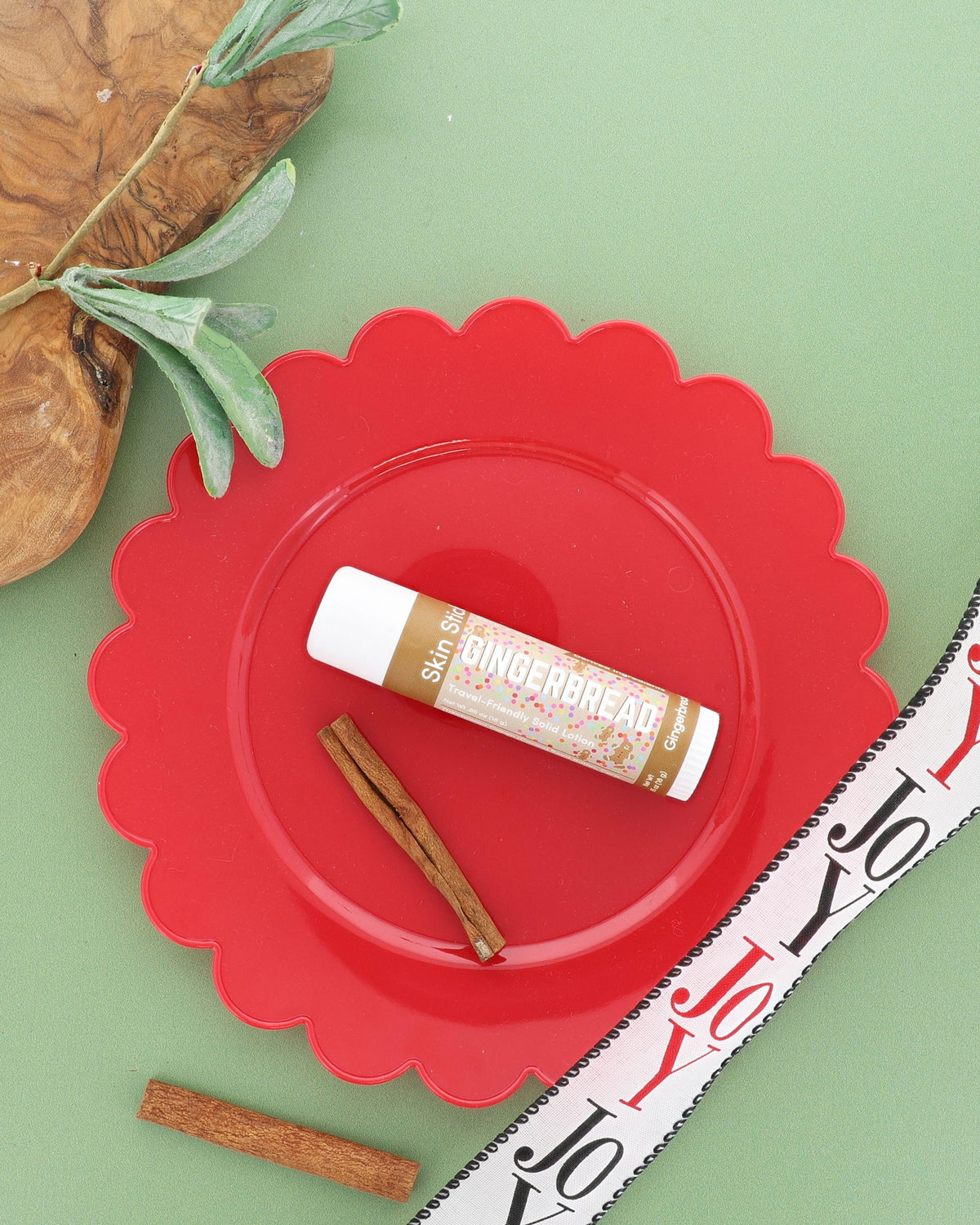 Gingerbread Skin Stick on a red scalloped plate with cinnamon sticks and a JOY ribbon, wide sage green frame