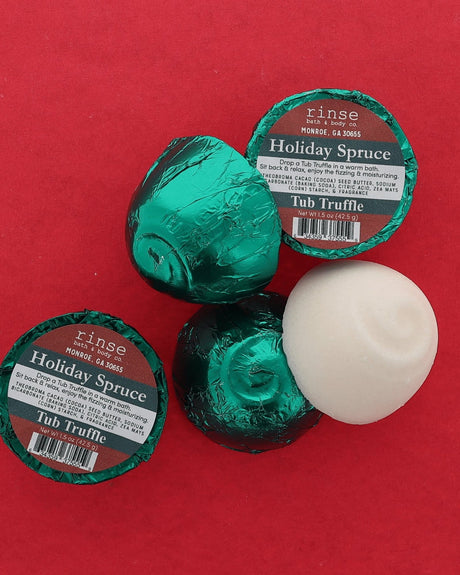 Two green foil-wrapped Holiday Spruce Tub Truffles and one unwrapped white dome on a deep red background — fresh evergreen for a winter bath. Rinse Bath & Body Co.