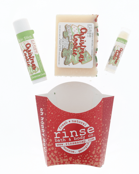 The Christmas Cookie set from the holiday assortment laid out flat — bar soap, solid lotion skin stick and lip balm above the red carton. Rinse Bath & Body Co.