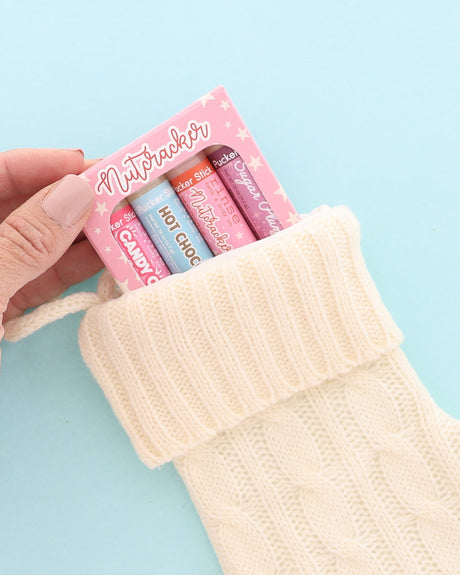 Pink Nutcracker lip balm pack tucked into a cream knit stocking on light blue