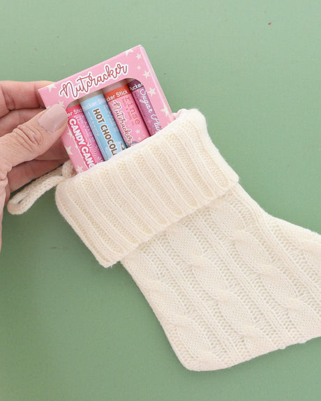 Pink Nutcracker lip balm pack tucked into a cream knit stocking on sage green