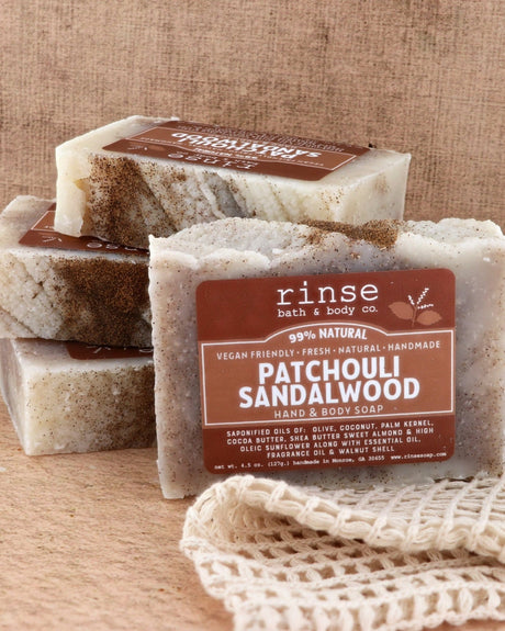 Patchouli Sandalwood bars stacked and styled, cocoa-dark tops catching the light — earthy patchouli over warm sandalwood. Rinse Bath & Body Co.