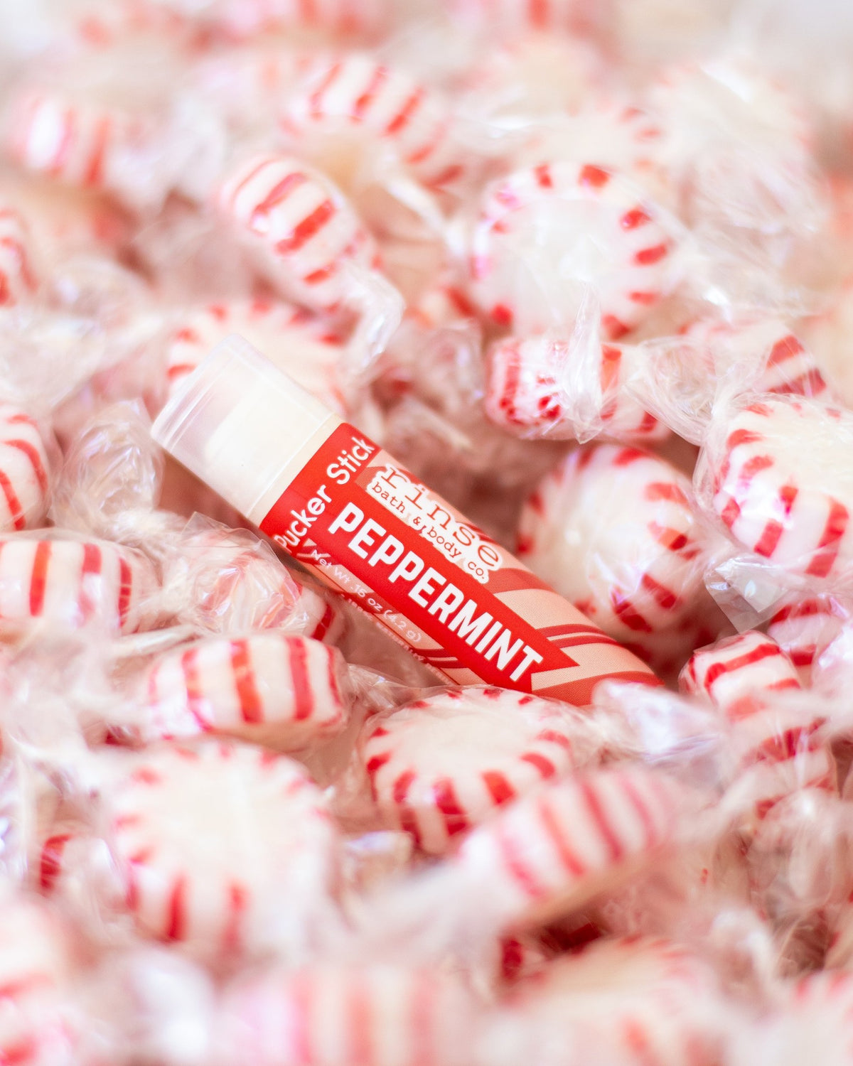 Peppermint Pucker Stick resting on red-and-white starlight mints — mint lip balm close-up