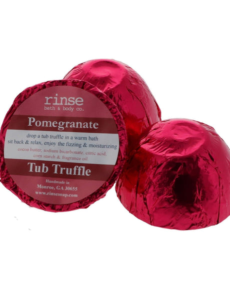 A magenta foil-wrapped Pomegranate Tub Truffle beside a second one cut open to show the cocoa butter dome, on white — tart, deep and a little dramatic. Rinse Bath & Body Co.