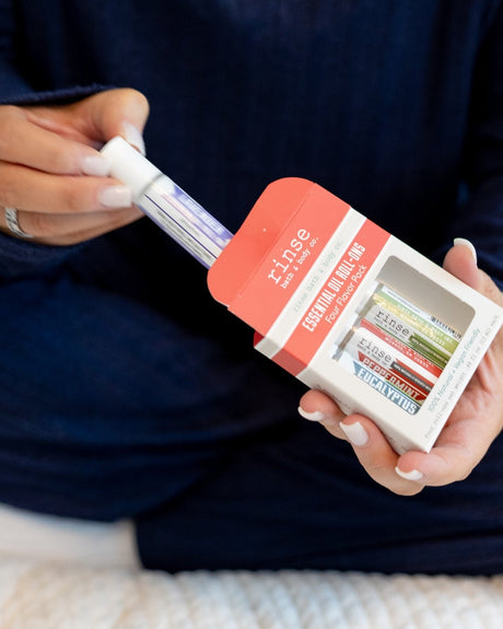 Hands sliding a roll-on from the Four Flavor Pack box — navy sweater sleeves in soft white light