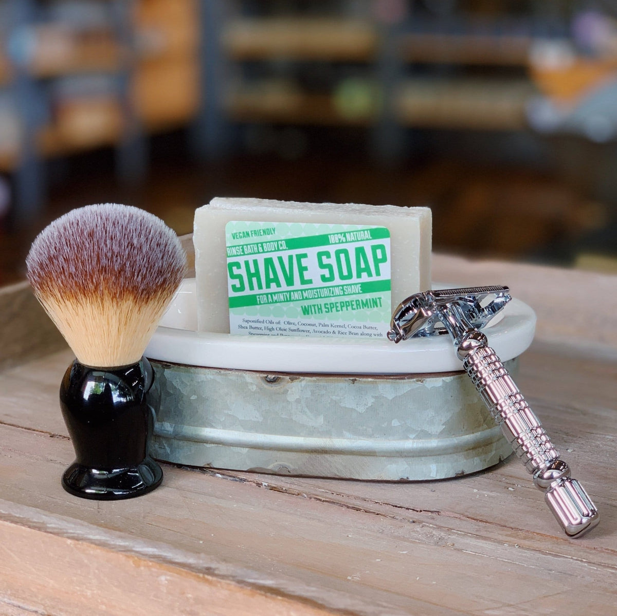 Speppermint Shave Soap sits in a distressed metal tub beside a brush and safety razor on light wood.