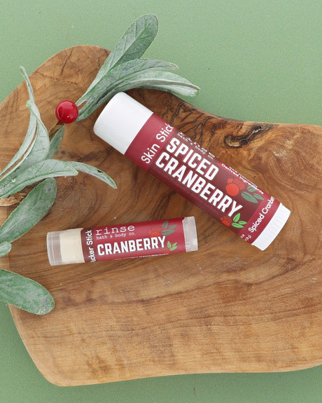 Spiced Cranberry Skin Stick and Cranberry Pucker Stick on an olive wood board with a frosted greenery sprig