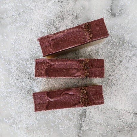 Three Sugared Fig soap tops on coarse white crystals — deep plum swoops with dried botanical seeds