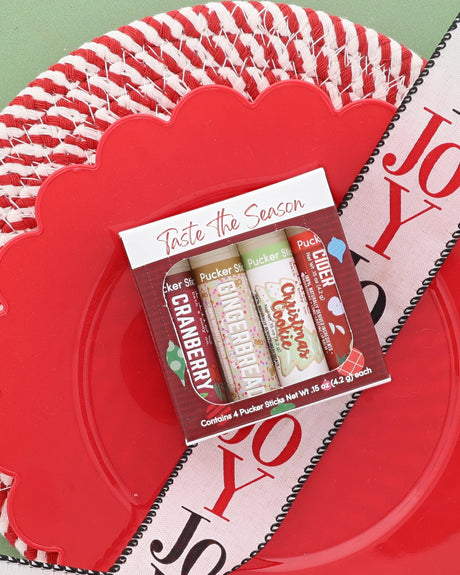 Taste the Season lip balm pack with Christmas Cookie, Cranberry and Gingerbread Pucker Sticks on a red woven plate with a JOY ribbon