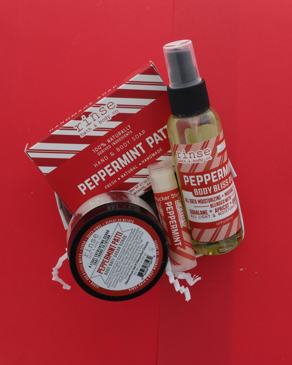 A gift set of five 'Since Nature' peppermint products arranged on a bright red background, including a hand and body soap bar, a peppermint body spray, a peppermint lip balm, a peppermint soap bar, and a peppermint hand and body soap box.