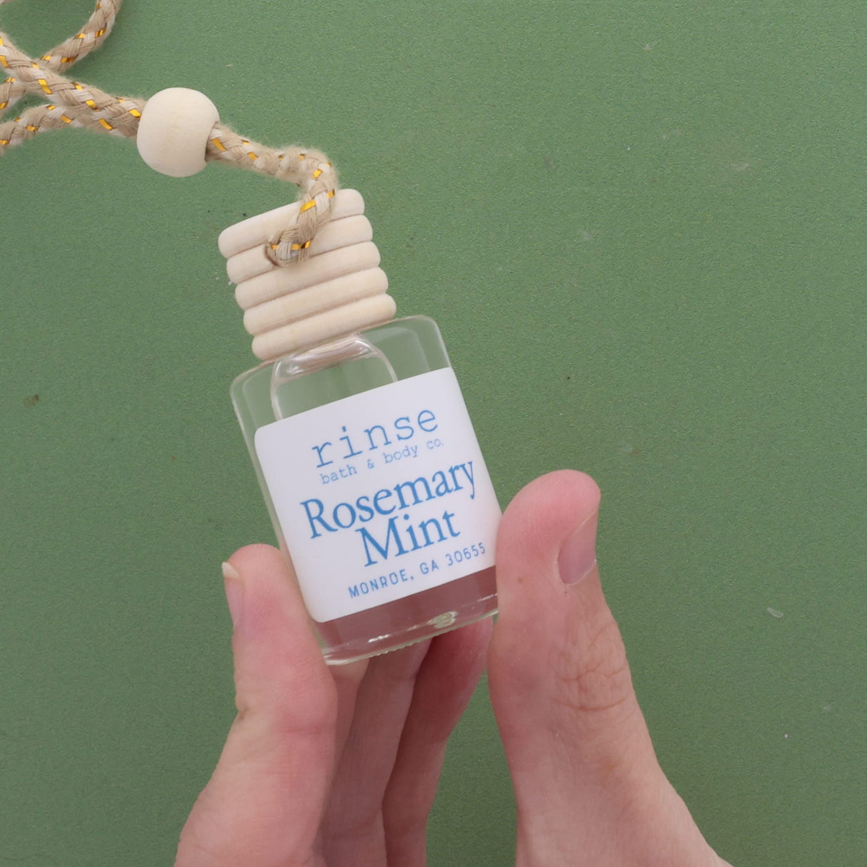 Hand holding a small bottle labeled 'Rosemary Mint' against a green background