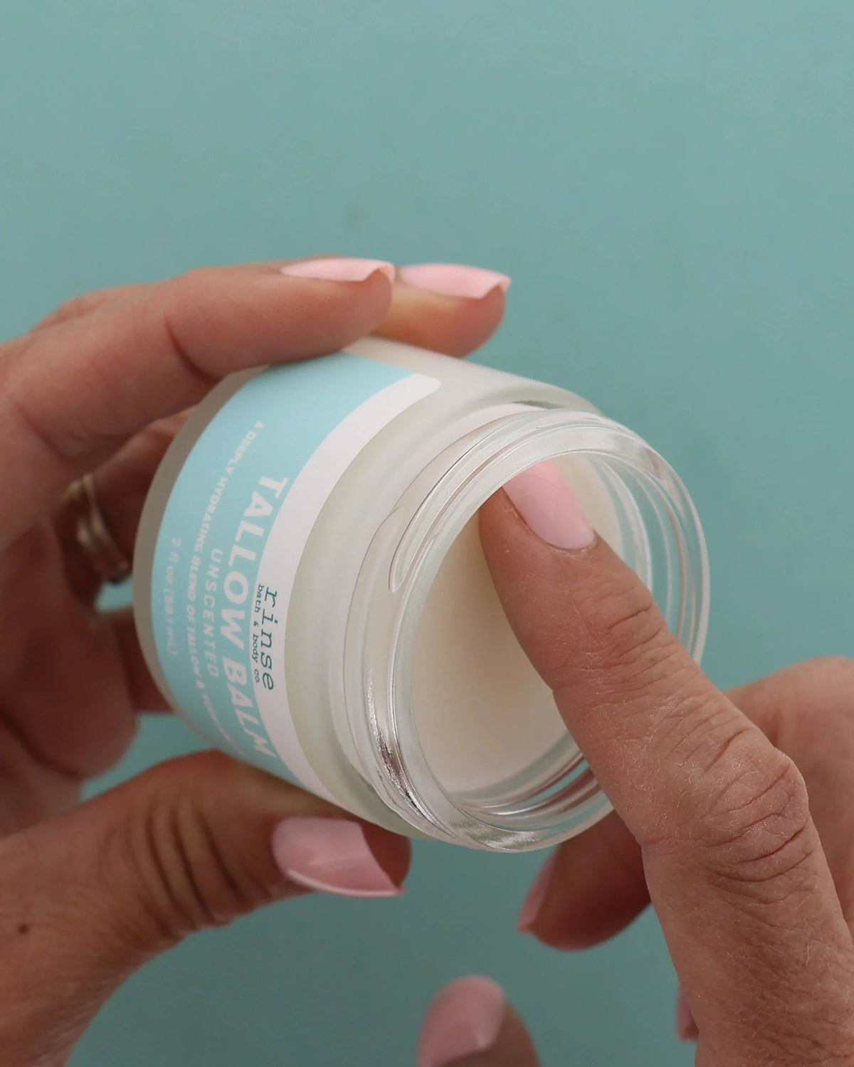 Two hands lifting the lid from a jar of Unscented Tallow Balm against a teal background — no essential oils, no fragrance. Rinse Bath & Body Co.