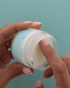 Two hands lifting the lid from a jar of Unscented Tallow Balm against a teal background — no essential oils, no fragrance. Rinse Bath & Body Co.