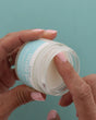 Hand dipping into a jar of unscented tallow against a teal background