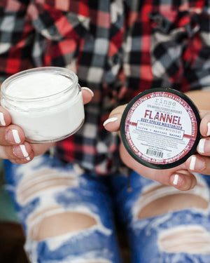 Flannel body spread in its tub with the lid off — a thick shea-butter moisturizer in sharp musk and clean cotton. Rinse Bath & Body Co.