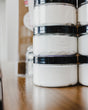 Almond & Honey body spread in its tub with the lid off — a thick shea-butter moisturizer for skin that drinks lotion and asks for more. Rinse Bath & Body Co.