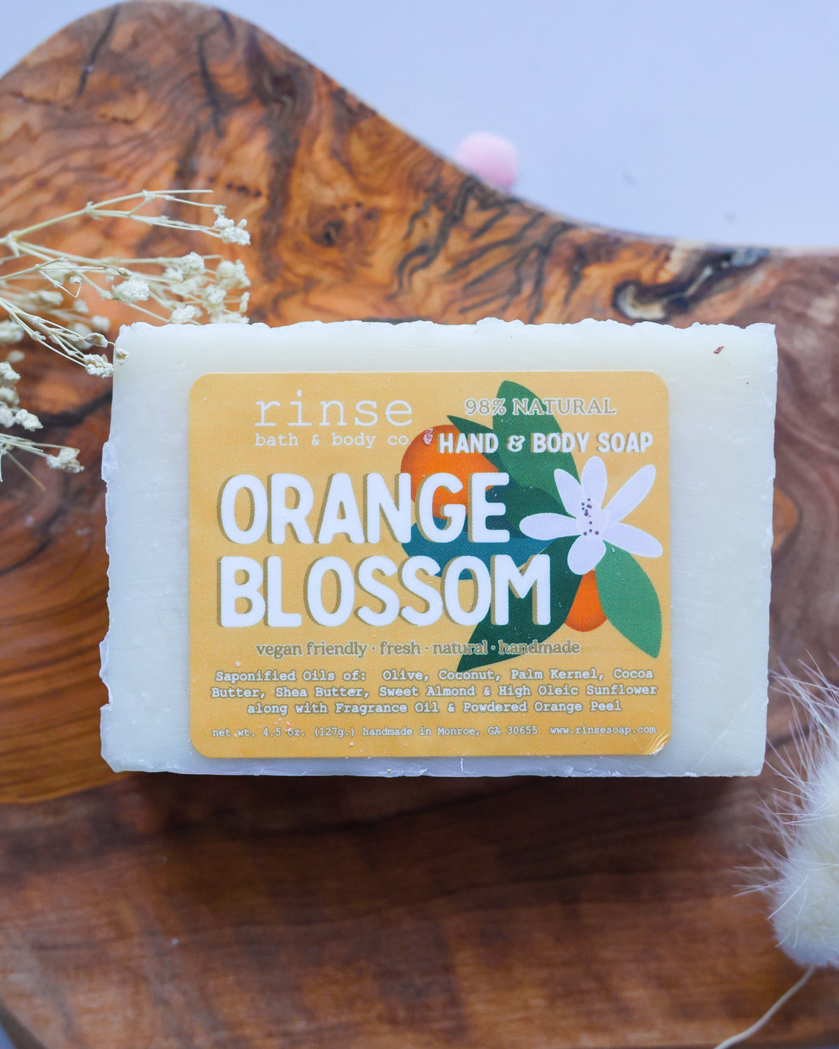 Orange Blossom soap rests on a dark rustic wood slab — dried baby's breath in soft gray light