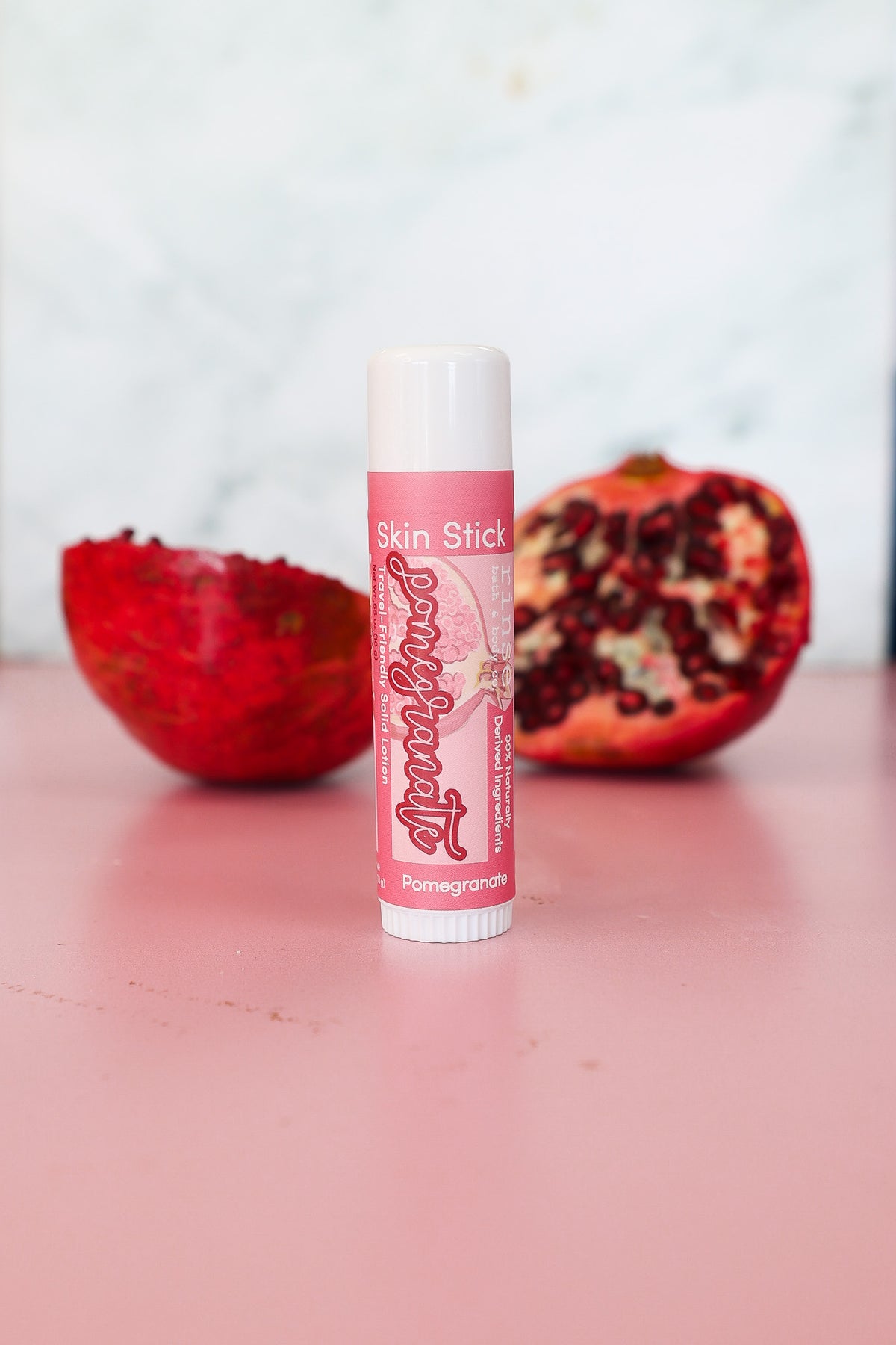 Tall Pomegranate Skin Stick standing on dusty rose — soft-focus pomegranate halves and marble wall