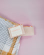 Cashmere soap nestles on a mustard plaid towel — orange-yellow marble against pale pink wall