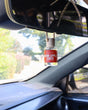Warm Apple Cider car diffuser in use, the wooden cap soaking up the oil before it hangs — one fill scents the car for weeks. Rinse Bath & Body Co.