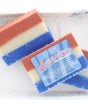 Two America the Beautiful soap bars resting on pale marble — layered red, cream, and cobalt catching clean daylight