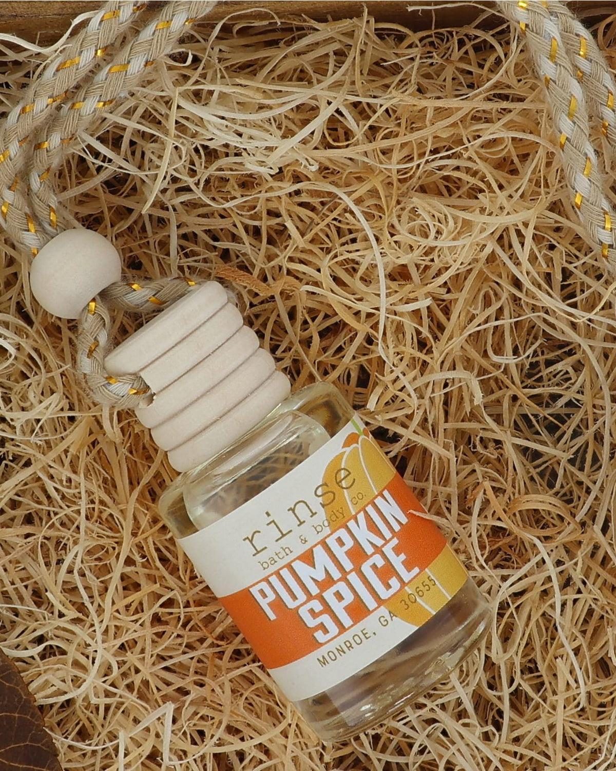 Pumpkin Spice car diffuser resting on excelsior in a wooden crate with dried autumn leaves on a warm tan backdrop