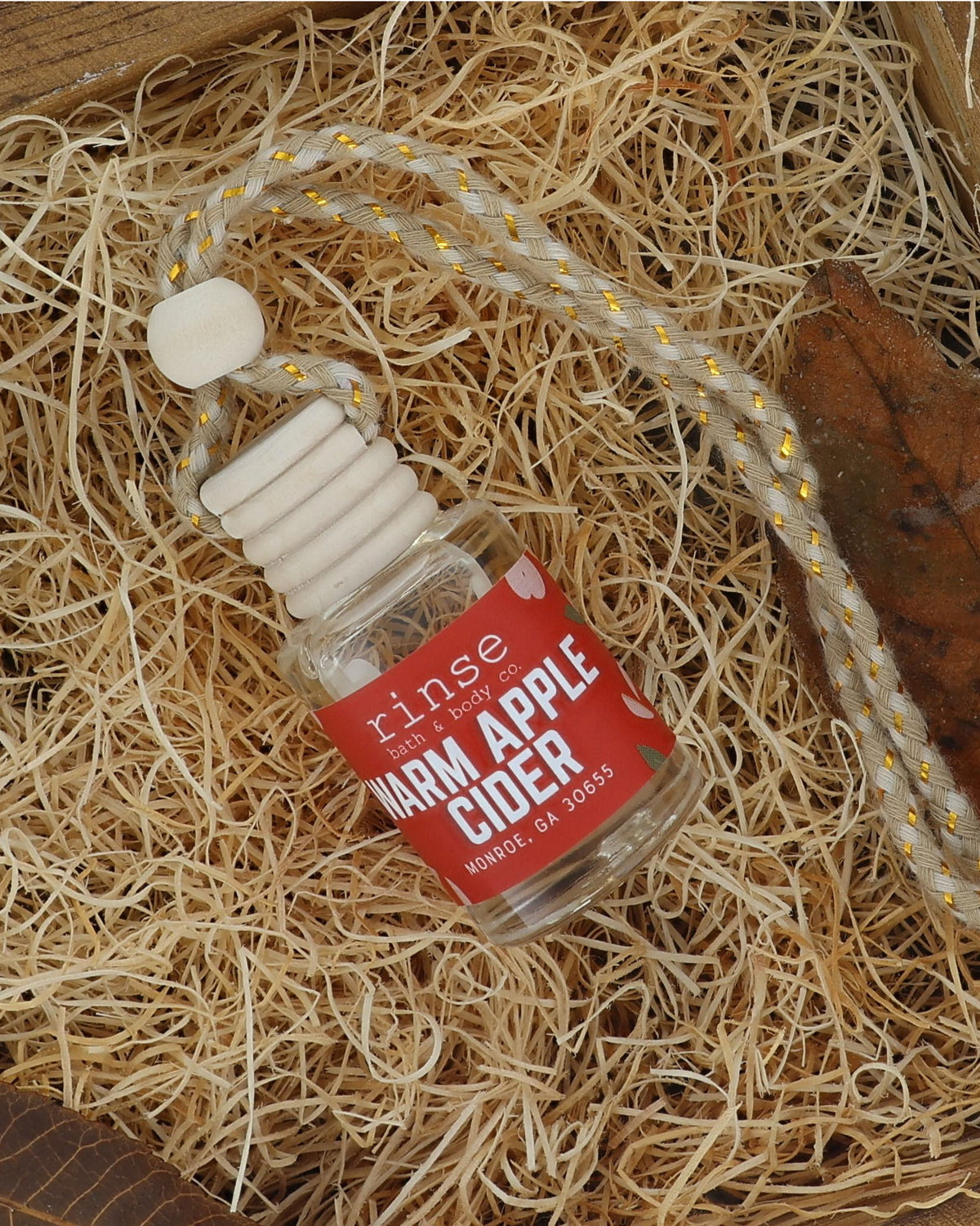 Warm Apple Cider car diffuser on excelsior in a wooden crate with a dried autumn leaf and cinnamon tones