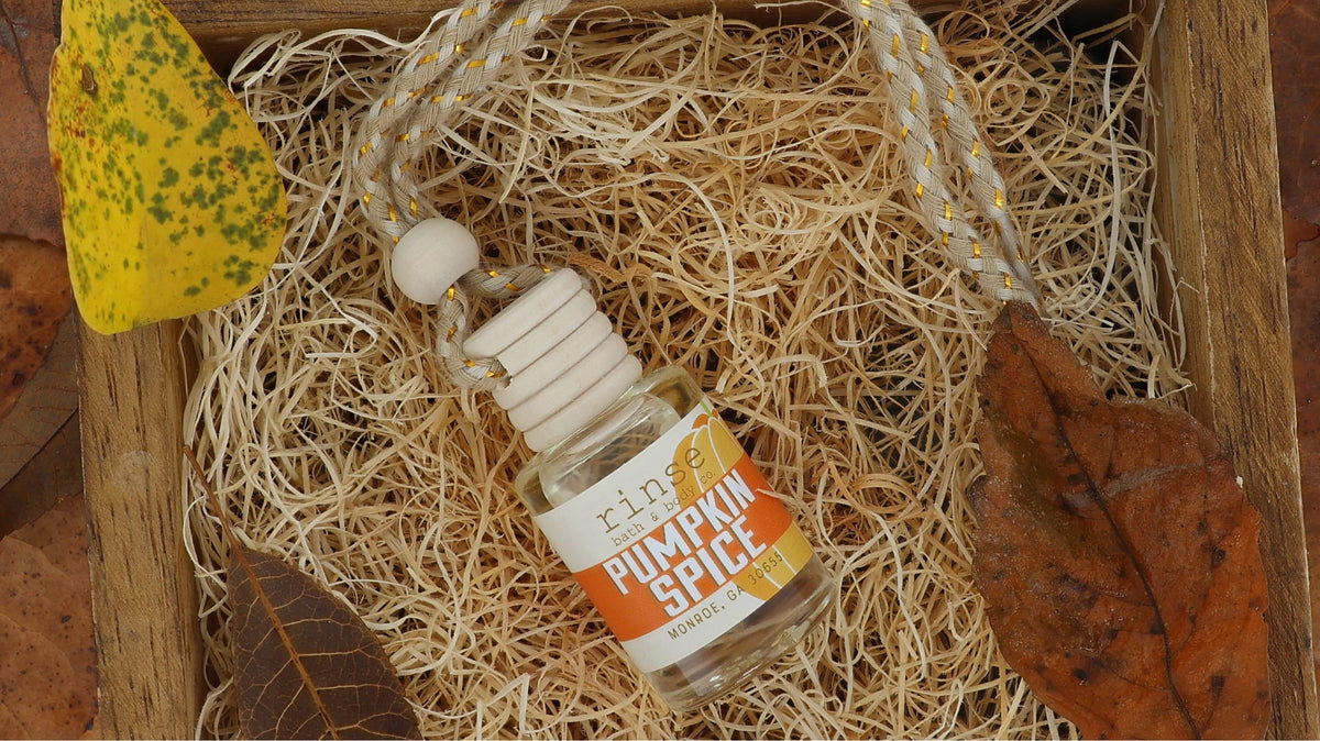 Pumpkin Spice car diffuser with its braided cord, tucked in straw with autumn leaves in a wooden crate