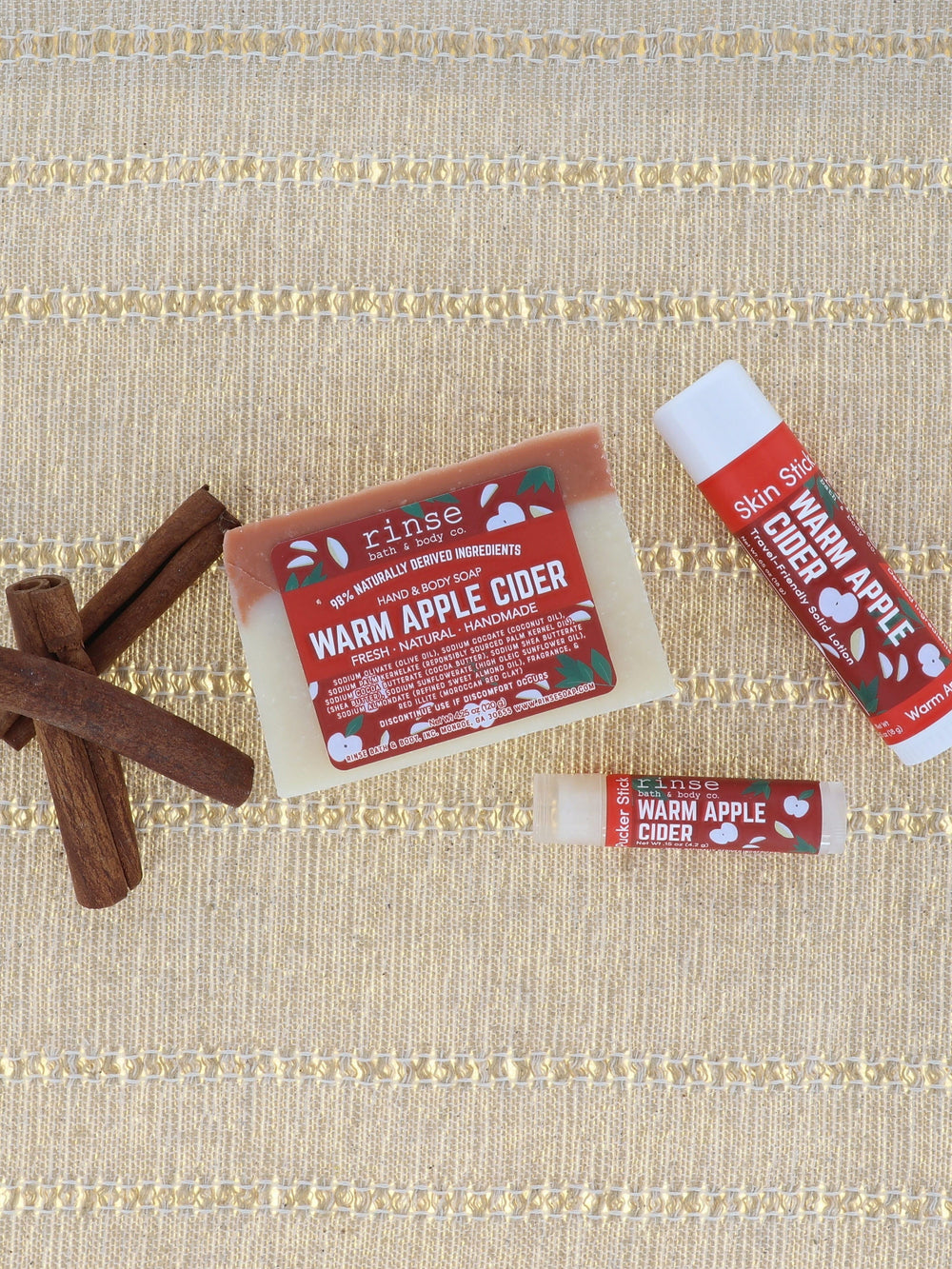 Warm Apple Cider bar soap styled with whole apples and cinnamon sticks on warm wood — spiced apple, clove and brown sugar, the bar that smells like the first cold morning. Rinse Bath & Body Co.